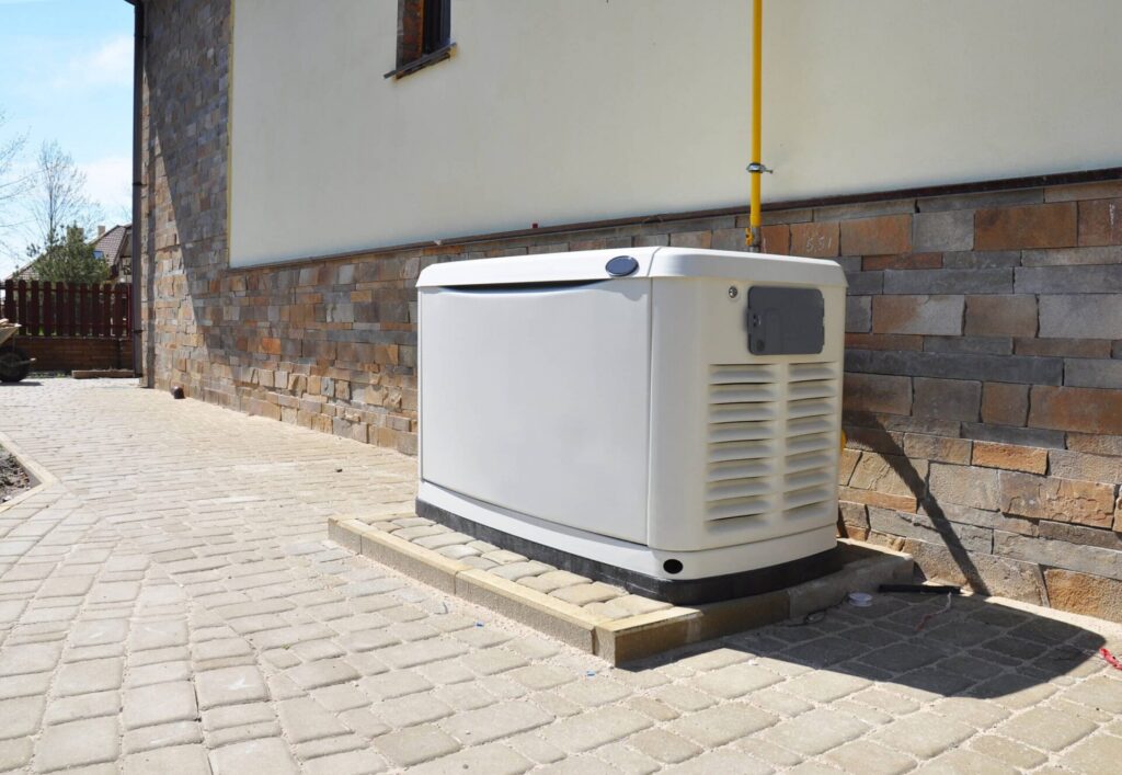 White residential standby generator unit mounted on a concrete pad against a brick foundation of a home.
