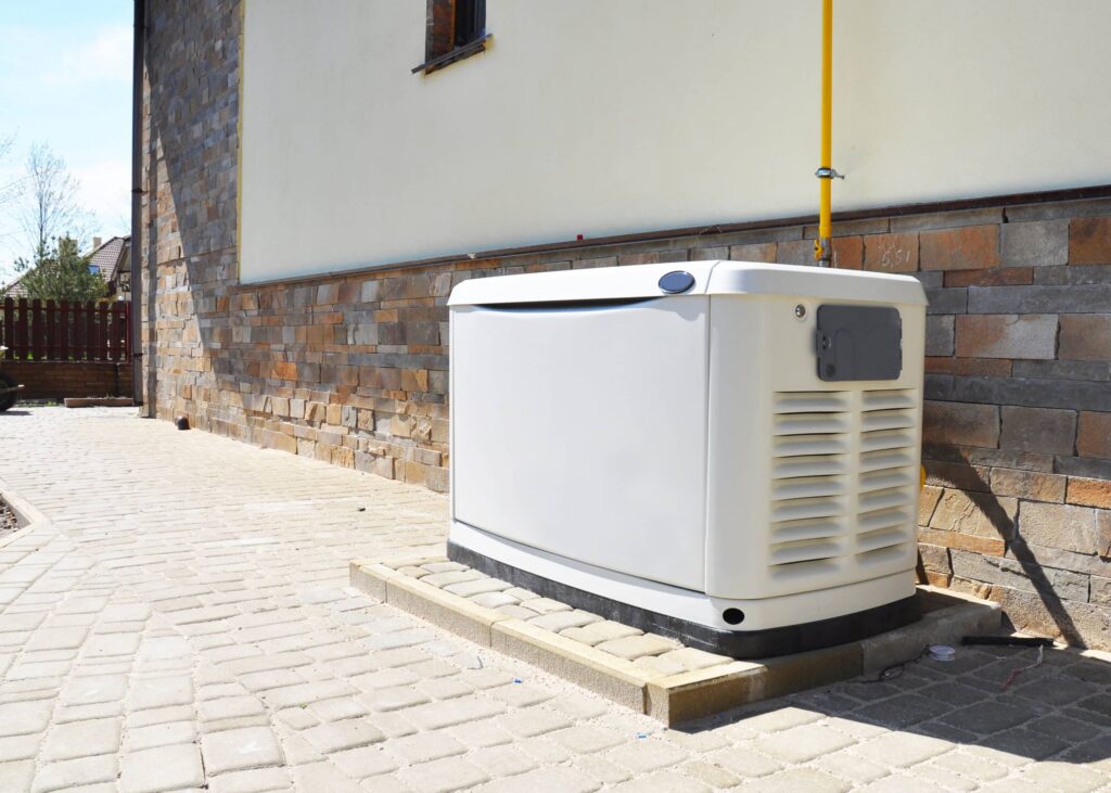 White residential backup generator unit installed on concrete pad against brick foundation of home with yellow gas line visible.