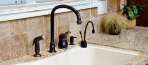 Modern black faucet and soap dispenser installed on a granite countertop with tile backsplash in a kitchen setting.