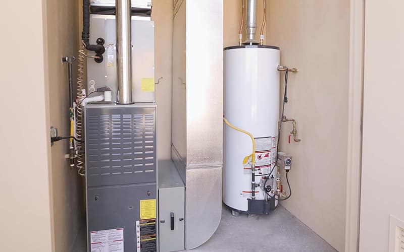 Interior utility room with gas furnace on left and white water heater on right, connected by copper piping and yellow safety straps.