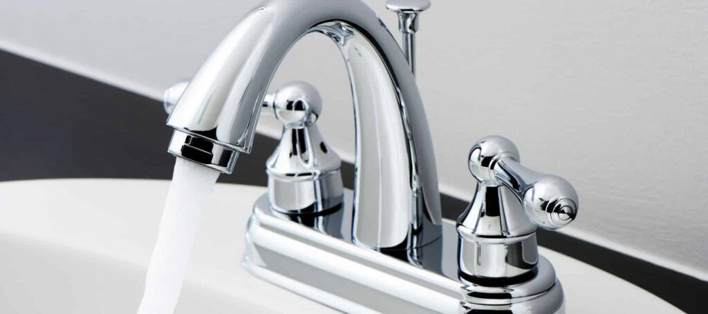 Polished chrome bathroom faucet with arched spout and dual lever handles installed on white sink basin.